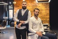 Man sitting on chair in barbershop with his master hairdresser.
