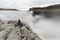 Man sitting on the cliff edge next to Dettifoss waterfall in Vatnayokull national park, Iceland