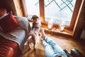 Man sitting in comfortable chair opposite big window in cozy country home and his beagle dog watching in wide window. Countryside