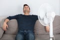 Man Sitting On Couch Cooling Off With Fan
