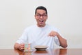 A man sitting on dinning table pointing to empty plate with excited expression Royalty Free Stock Photo