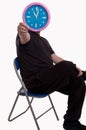Man sitting down on a chair and holding in front of his face a large wall clock showing time Royalty Free Stock Photo