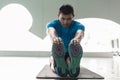 Man sitting down on exercise mat while touching his toes during stretching