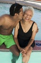 Man sitting on edge of swimming pool kissing mother on cheek elevated view.