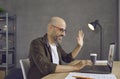 Man starting virtual business meeting and waving hello at screen of laptop computer