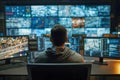 Man sitting in front of multiple monitors displaying traffic and data surveillance footage in a high-tech security control room Royalty Free Stock Photo
