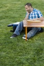 Man sitting on the grass at a picnic table with a cooler.