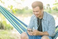 Man sitting on hammock and using smartphone with white earphone. Outdoor shooting with morning sunlight effect