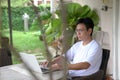 Man sitting at his house patio with garden view, working on his laptop. Work from home concept