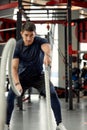 Man sitting on his toes holding a pair of battle ropes for workout. guy at the gym working out with fitness rope.