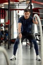 Man sitting on his toes holding a pair of battle ropes for workout. guy at the gym working out with fitness rope.