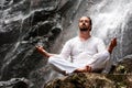 Man sitting in meditation yoga on rock at waterfall in tropical