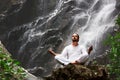 Man sitting in meditation yoga on rock at waterfall in tropical Royalty Free Stock Photo