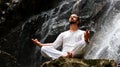 Man sitting in meditation yoga on rock at waterfall in tropical