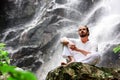 Man sitting in meditation yoga on rock at waterfall in tropical Royalty Free Stock Photo