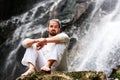 Man sitting in meditation yoga on rock at waterfall in tropical