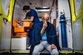 Man sitting with an oxygen mask in an ambulance car, a nurse looking for some supplies in her medical kit Royalty Free Stock Photo