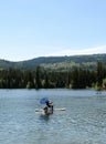 Man sitting and paddling under umbrella on mounting beach chair on top of SUP paddle board in the middle of Heffley Lake near Sun Royalty Free Stock Photo