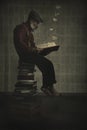 Man sitting on a pile of books reading a book letting go of the imagination Surreal image. Vertical image Royalty Free Stock Photo