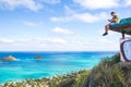 Young man sitting on pillbox over looking Lanikai texting on a c