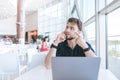 Man is sitting at a restaurant near the window, working on a laptop, talking on the phone and looking away Royalty Free Stock Photo