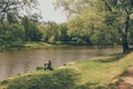 Man sitting on river bank is fishing among lush park greenery