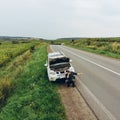 Man sitting on road near broken car. trying stop car for help