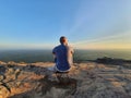 A man sitting on a rocky cliff overlooking the plains below at Preah Vihear temple on the border of Thailand and Cambodia