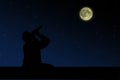 The man sitting on the roof and looks through binoculars at the full moon night