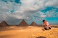 Man sitting on the sandy desert dunes posing in front of the great pyramids of giza. Traveling egypt in winter time, tourists Royalty Free Stock Photo