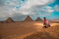 Man sitting on the sandy desert dunes posing in front of the great pyramids of giza. Traveling egypt in winter time, tourists Royalty Free Stock Photo