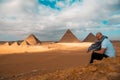 Man sitting on the sandy desert dunes posing in front of the great pyramids of giza. Traveling egypt in winter time, tourists Royalty Free Stock Photo