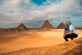 Man sitting on the sandy desert dunes posing in front of the great pyramids of giza. Traveling egypt in winter time, tourists Royalty Free Stock Photo