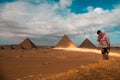 Man sitting on the sandy desert dunes posing in front of the great pyramids of giza. Traveling egypt in winter time, tourists Royalty Free Stock Photo