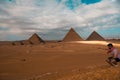 Man sitting on the sandy desert dunes posing in front of the great pyramids of giza. Traveling egypt in winter time, tourists Royalty Free Stock Photo