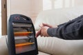 Man sitting on sofa with electric heater near his hands