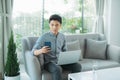 Man sitting on sofa with his laptop teleworking from home, wearing headphones and looking at the mobile phone Royalty Free Stock Photo