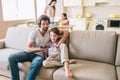 Man is sitting on sofa with his son and read a book for him aloud. Boy looks at it. Woman and girl are cooking in Royalty Free Stock Photo