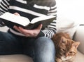 Man sitting on sofa reading a book with ginger cat relaxing next to him Royalty Free Stock Photo