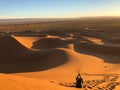 Man sitting on sun dunes at a desert surrounded by tracks Royalty Free Stock Photo