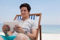 Man sitting on sunlounger and using digital tablet on the beach Royalty Free Stock Photo