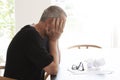 Man sitting at a table and hiding his head in despair. A pair of glasses lying on a pile of papers with some crumpled papers on t