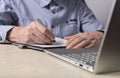 Man sitting at table with laptop and writing with pen in diary. Hands closeup. Taking online courses, preparation for