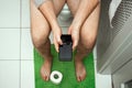 A man sitting on the toilet holding a smartphone in his hands, top view. The concept of problems with the chair, intestines, Royalty Free Stock Photo