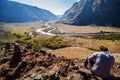 A man sitting on top with a view of the valley of a mountain river