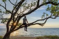 Man sitting on the tree watching sunset over the sea, enjoying a peaceful moment Royalty Free Stock Photo