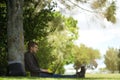 Man sitting under a tree, reposing and working on his computer. You can see his backpack next to him.