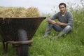 Man sitting beside wheelbarrow with hay in field portrait
