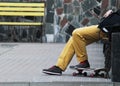 Man Skateboarder in yellow jeans relaxing on bench. Yellow bench and stone background. Lifestyle Relax Hipster Concept Royalty Free Stock Photo