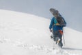 man with ski equipment and a snowboard climbs a snowy mountain. Blue sky and snowy mountain in the background. Royalty Free Stock Photo